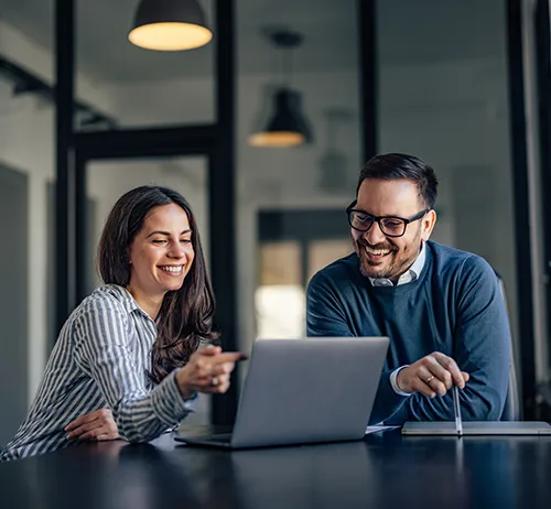 firm-valuation-thumbnail Two professionals smiling and collaborating on a laptop in a modern office